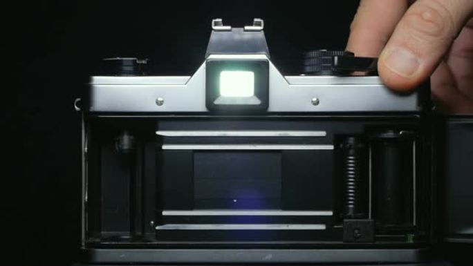 单反胶片相机的窗帘打开，让光线照射到胶片上，同时手按下快门按钮