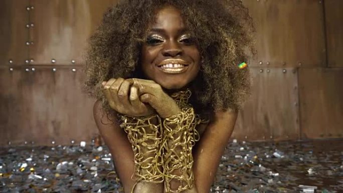 特写性感的非洲裔美国女模特与金色光泽的化妆品包围着银色的彩纸面部艺术。演播室背景