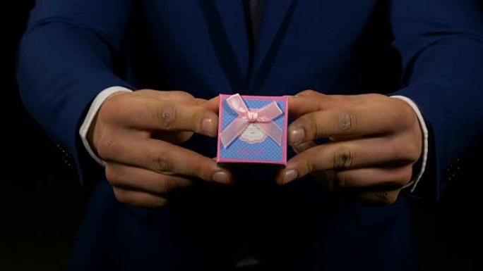 一个男人的手展示并拿着小礼物首饰盒