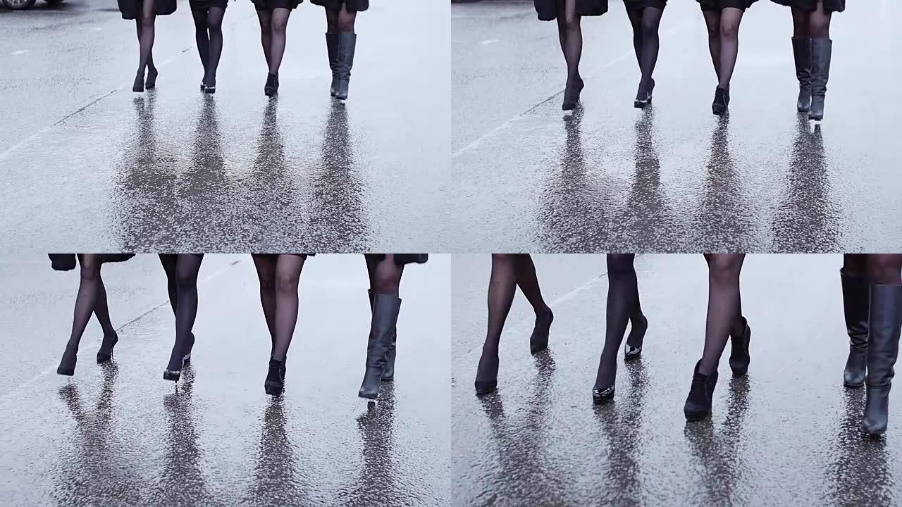 穿着高跟鞋的四个女人的腿在湿沥青上步履蹒跚。慢动作