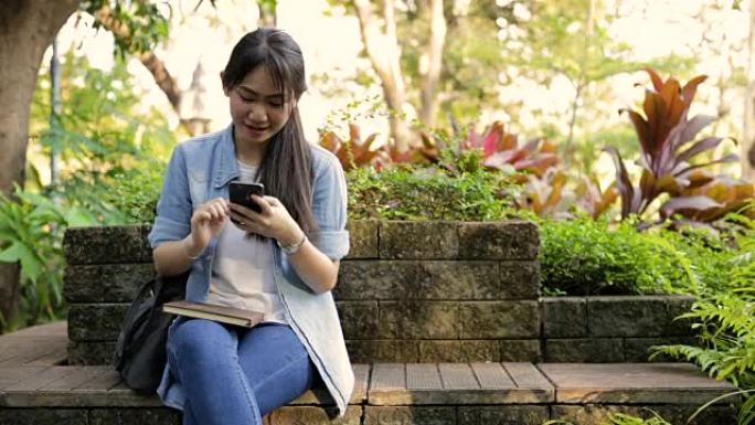 年轻的亚洲女孩在公园里快乐地使用智能手机
