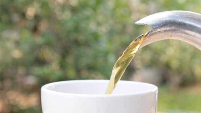 热茶倒入绿树背景上的白色茶杯特写