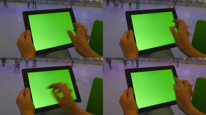 在购物中心使用绿屏平板电脑的女性双手。很多人在后台的室内溜冰场上滑冰