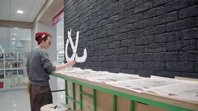 年轻女画家在咖啡店的黑砖墙上做白色设计