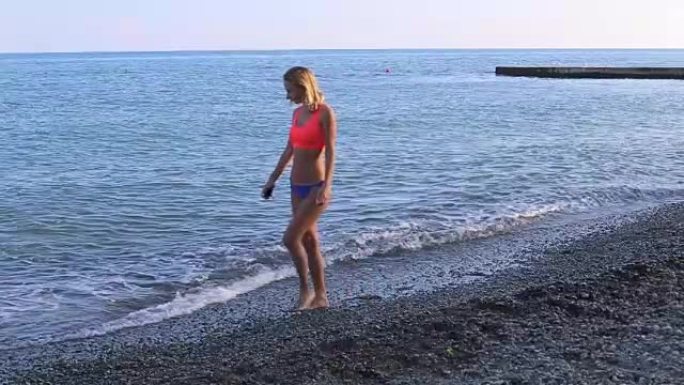 孤独的女孩沿着海滩散步，看着地平线。