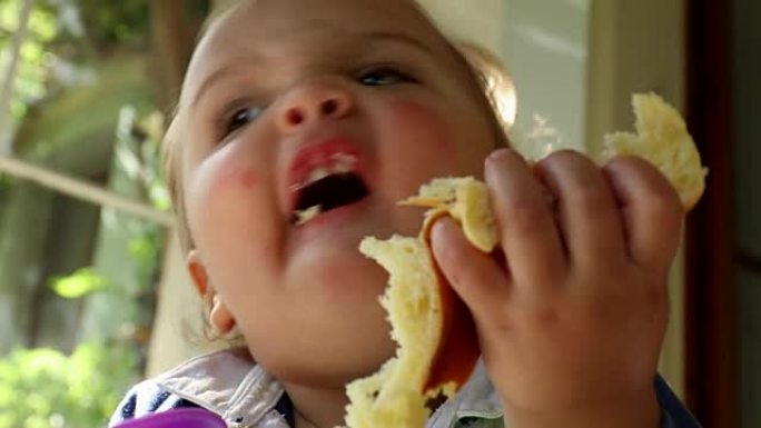 高脚椅上可爱的婴儿蹒跚学步的金发男孩的特写。婴儿吃蛋糕和玩婴儿玩具的肖像