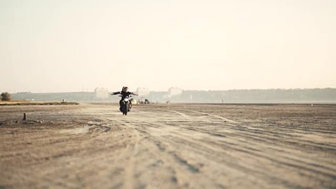 日落时分，两个美丽的女朋友在沙漠上没有手骑摩托车。女自行车手。慢动作