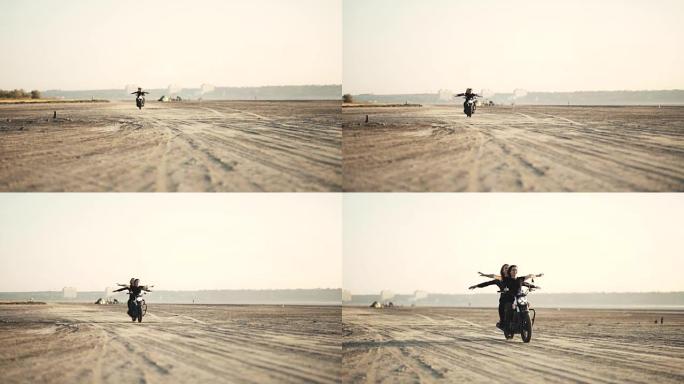 日落时分，两个美丽的女朋友在沙漠上没有手骑摩托车。女自行车手。慢动作