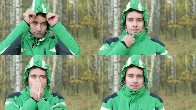 在寒冷的秋公园里，年轻英俊的男人戴着兜帽。他看着镜头。装备绿色运动夹克保暖