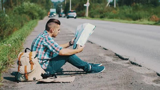 男人坐在乡下的路上。搭便车。等待帮助。查看地图