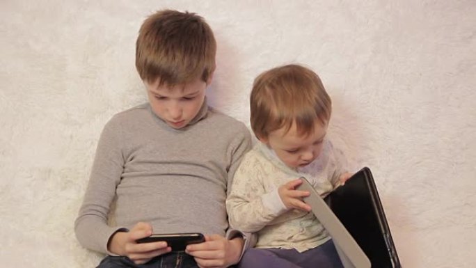 孩子们坐在沙发上玩你的平板电脑和手机