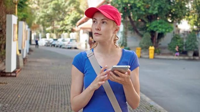 穿着红色帽子的迷人年轻旅游女性在智能手机上使用在线地图寻找正确的方向