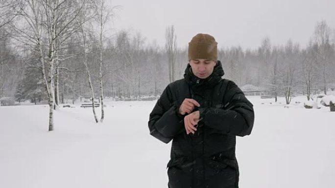 一名男子在冬季白雪皑皑的森林中检查智能手表上的信息。大雪。他口述对时钟的语音反应。一个穿着深色保暖夹