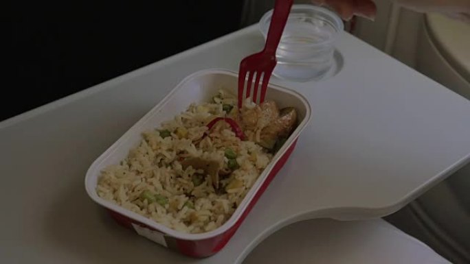 在桌子上的飞机上是一次性餐具，上面放了一盘米饭和鸡肉，一个女人用叉子吃饭