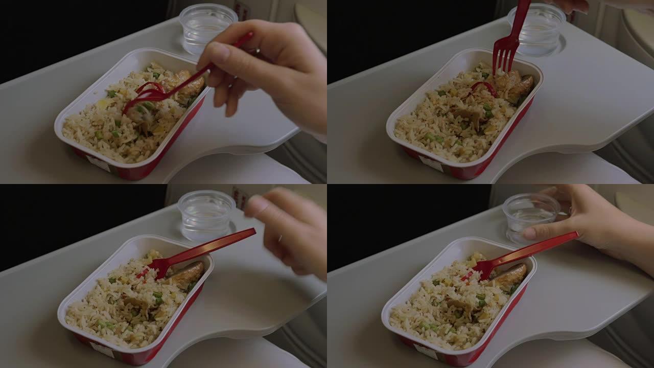 在桌子上的飞机上是一次性餐具，上面放了一盘米饭和鸡肉，一个女人用叉子吃饭