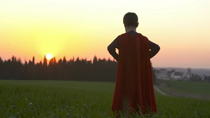 日落时，一个在绿色田野里穿着超级英雄斗篷的男孩