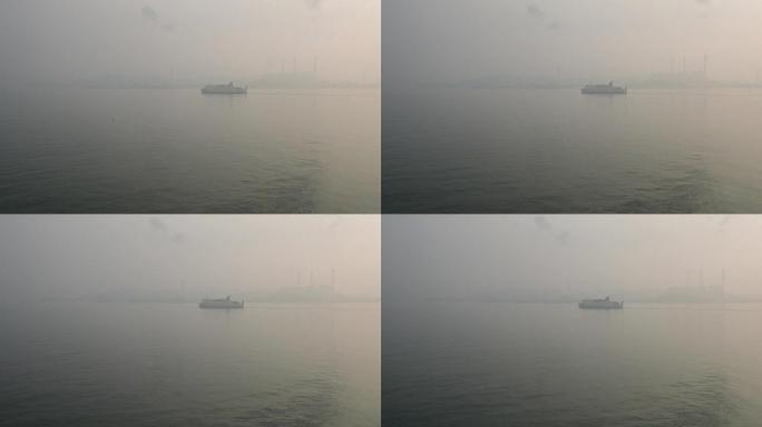 在雾蒙蒙的日子里，渡轮驶向韩国首尔仁川港，发电站和风力发电机的轮廓在雾中可见。