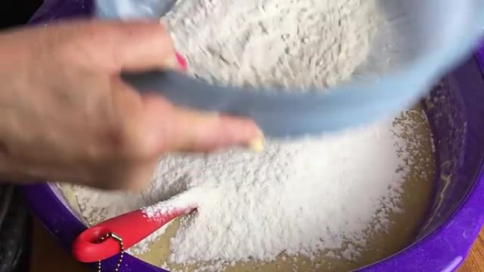 人的手在碗中通过筛子筛面粉。