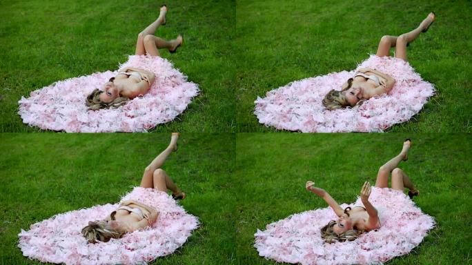 穿着粉色优雅连衣裙的年轻性感金发女孩躺在绿色草坪上