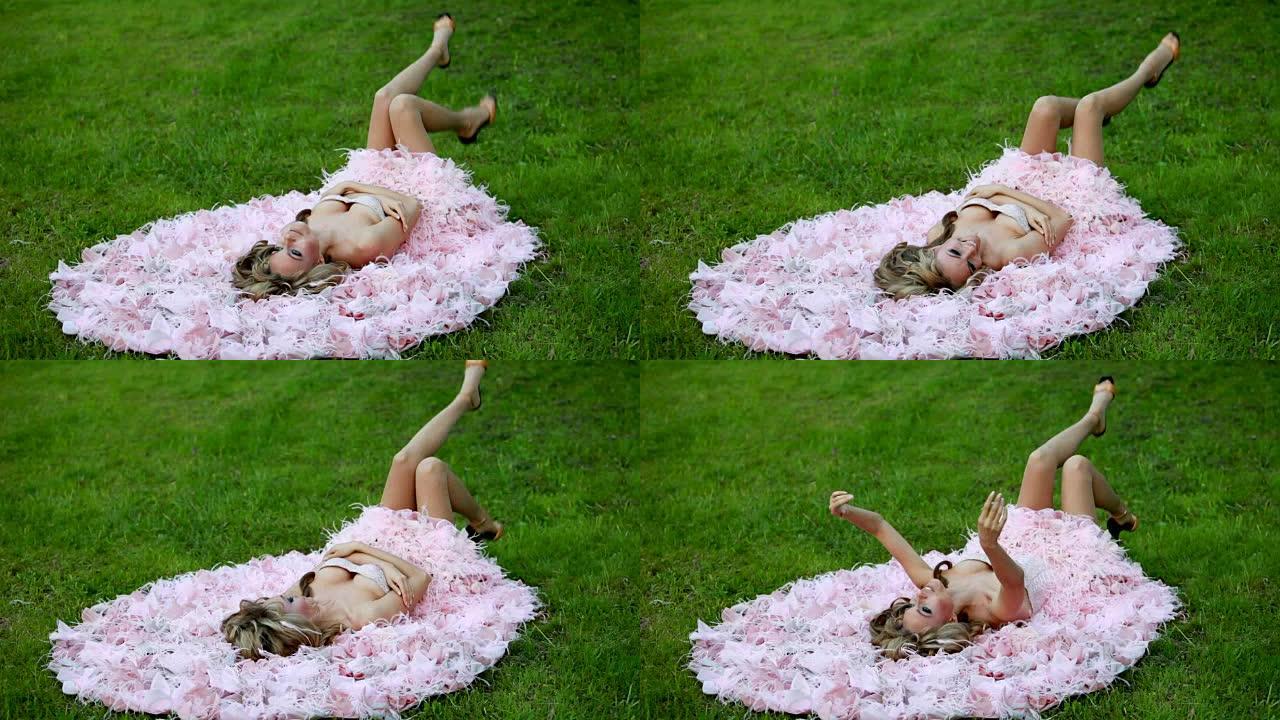 穿着粉色优雅连衣裙的年轻性感金发女孩躺在绿色草坪上