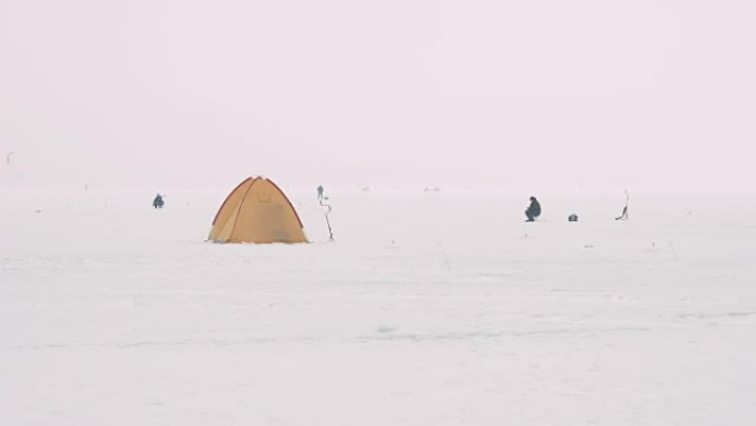 在冰冻的湖面上的看台上进行冬季钓鱼的帐篷。坐在附近的几个渔民