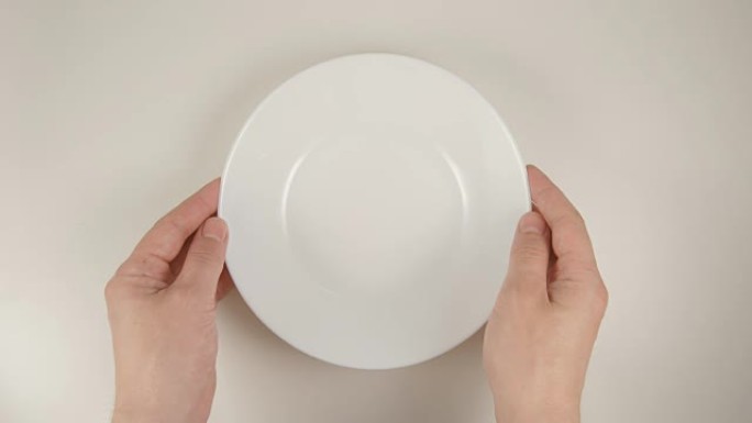俯视图: 人类的手在白色的桌子上放一个白色的盘子