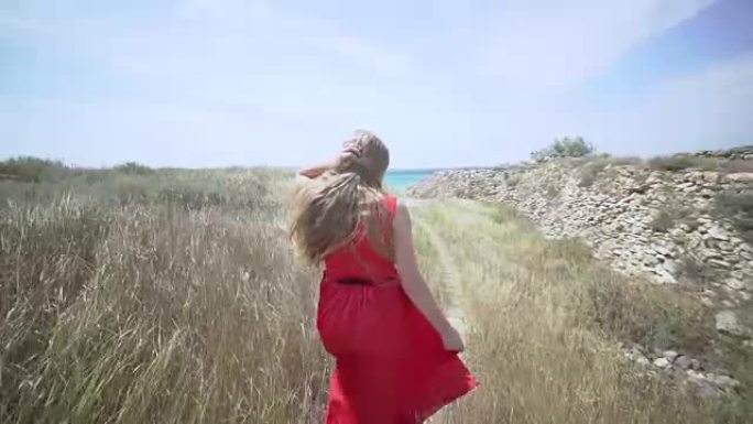 穿着红色连衣裙的年轻女孩赤脚走在通往大海的路上