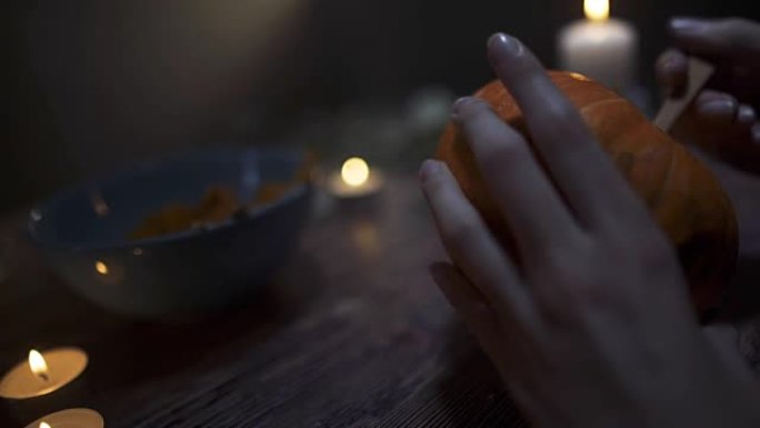 男性的手在晚上用蜡烛在木桌上sc出南瓜的种子和内容物。万圣节主题，杰克灯