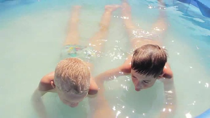 两个漂亮的小男孩温暖的夏日在游泳池里游泳，互相泼水