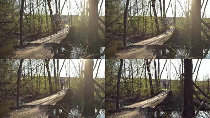 骑自行车的人在一座木桥上过河的公园里散步。慢动作