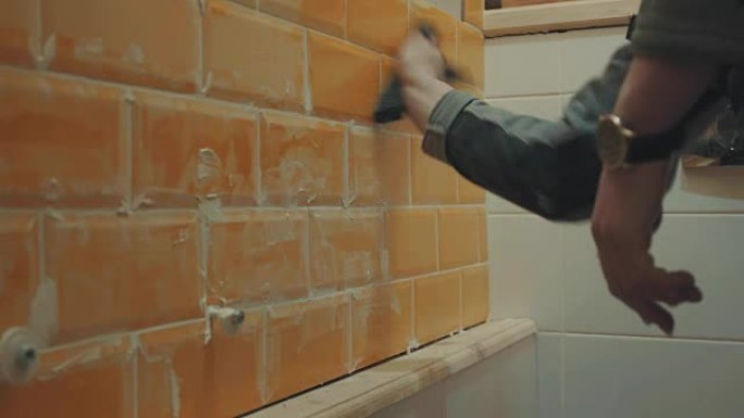 男人的手洗掉了墙上橙色瓷砖上的油灰残余物
