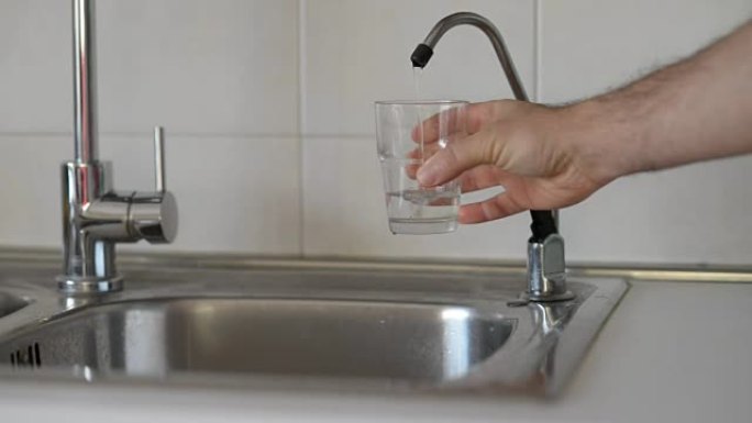 一个人从家庭过滤系统中倒出饮用水并装满玻璃杯。