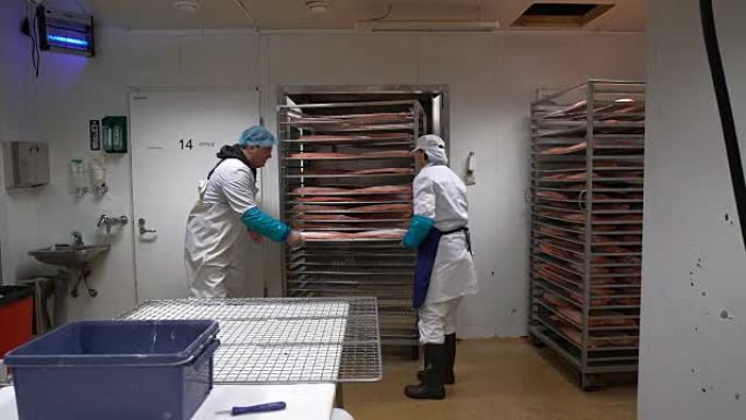 一名工人将鲑鱼片放入烤箱中，以便在工厂里抽烟。