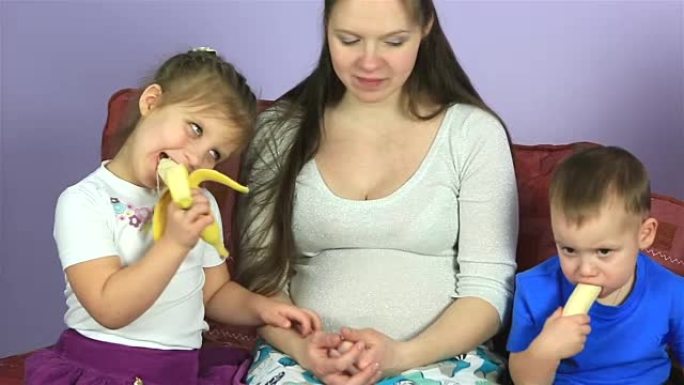 孕妇有年幼的孩子吃香蕉。幸福的家庭等待第三个孩子