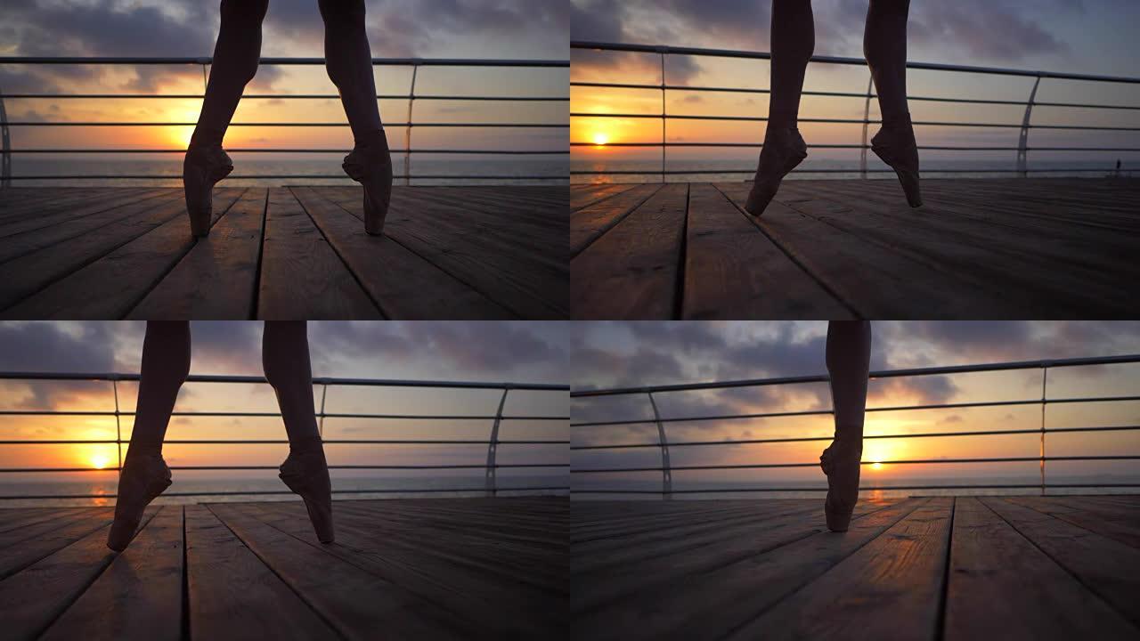 芭蕾舞演员的脚在海边或海洋附近的路堤上练习足尖练习时的特写镜头，日出背景，脚尖鞋中女人的脚部轮廓。芭