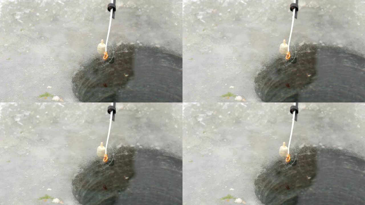 冰洞附近的冬季钓鱼用钓鱼竿。浮子在水中移动