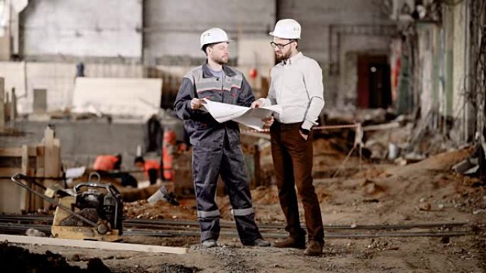 两名戴着安全帽的男子站在建筑区域，看着未来的建筑方案。工头指向图纸并向工人解释当前组装的亮点