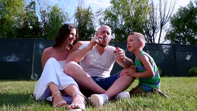 一个幸福家庭的肖像，一家人玩肥皂泡坐在草坪上，爸爸手里拿着泡泡