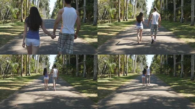 夫妻手牵着手，在热带公园散步。年轻的男人和女人沿着异国情调的公园巷，在棕榈树上观看。暑假旅行概念。后