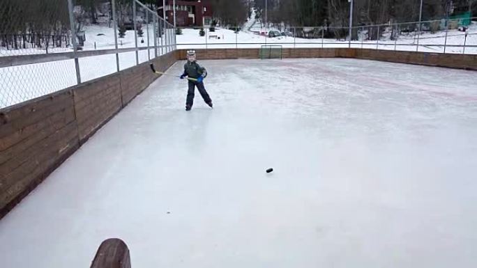 小男孩在冬季在溜冰场上学习打曲棍球