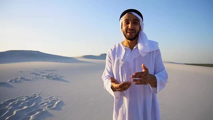 一个阿拉伯人站在广阔的沙漠中，在夏日的空旷中，看着镜头告诉我们信息，和我们握手