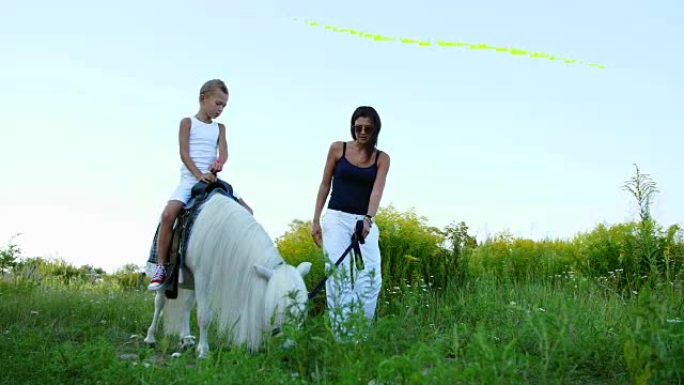 一个女人和一个男孩在田野里走来走去，儿子骑着小马，母亲拿着小马作为bri绳。快乐快乐的家庭假期。户外