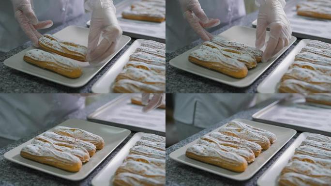 面包师用手将新鲜出炉的小饼和糖粉整齐地折叠在面包店厨房的漂亮白色盘子上。桌上有许多美味的蛋糕