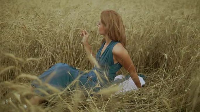 迷人的年轻女子坐在金色的麦田里。她的手在摸麦穗。收获概念。收获。慢动作镜头