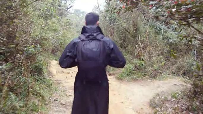 穿着雨衣的年轻人在旅行中走在木头小径上。背着背包徒步旅行的家伙走在热带潮湿的森林里。跟随男性游客踏上