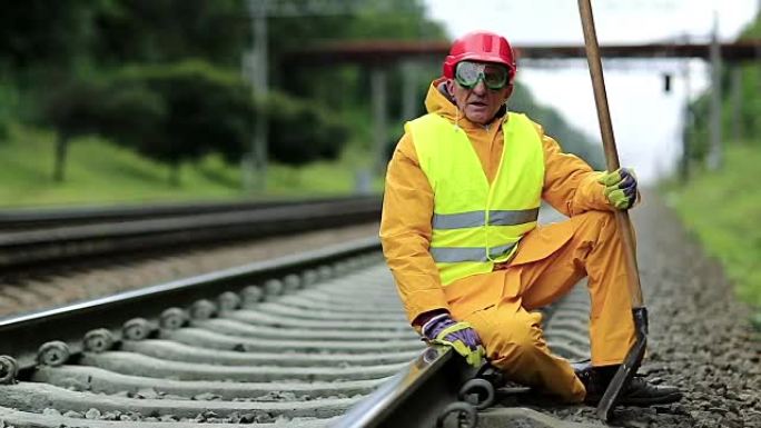 铁路工人穿着黄色制服，手拿铁铲坐在铁轨上