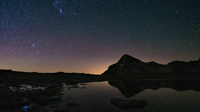 银河系的明显旋转和白雪皑皑的山脊以外的星空，反映在田园诗般的apine湖上。延时视频。