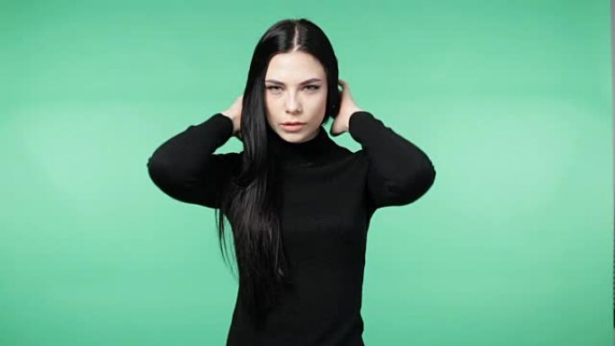 美丽的年轻黑发女人穿着黑色衬衫玩弄头发，微笑着看着相机，色度键绿色屏幕背景
