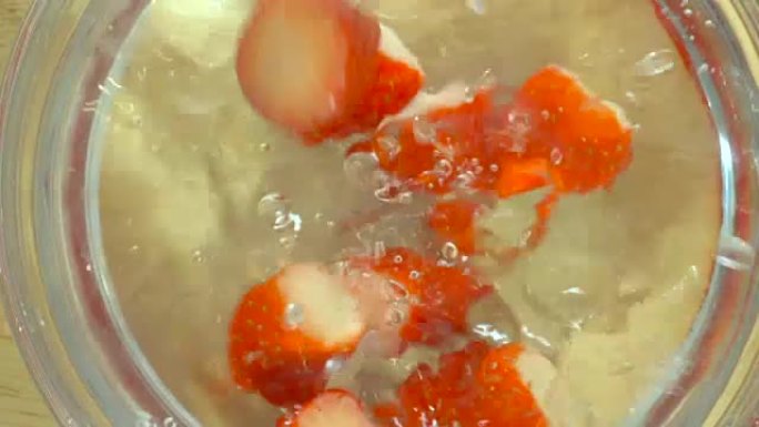 新鲜的红色草莓倒入一碗水中，缓慢