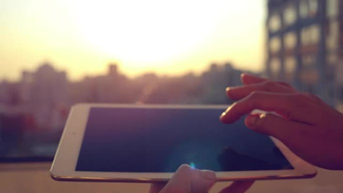 女人的手在城市模糊的日落剪影处使用平板电脑